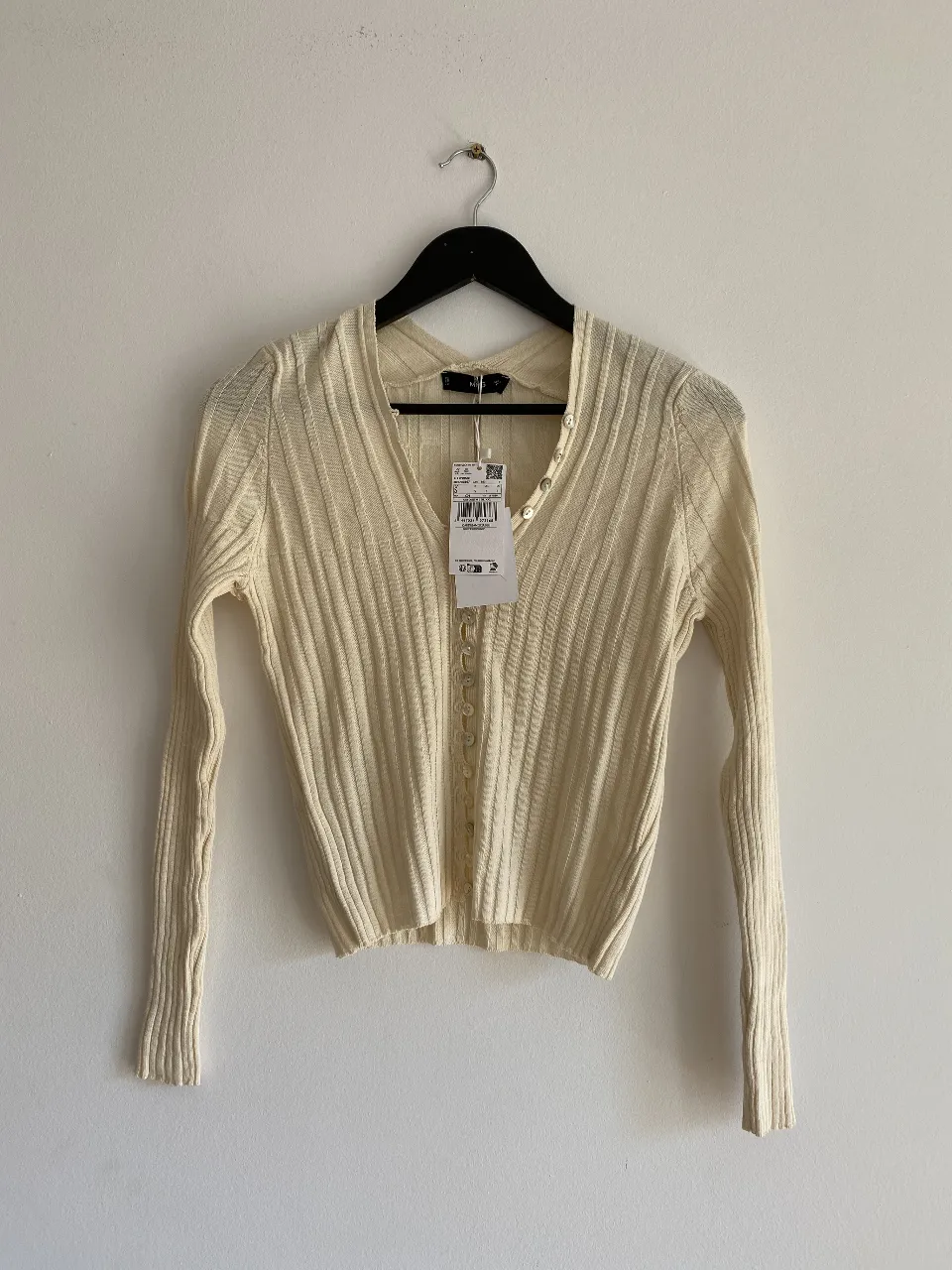 Cardigan tejido de punto, color crudo, con botones. Ideal para un look casual y elegante.