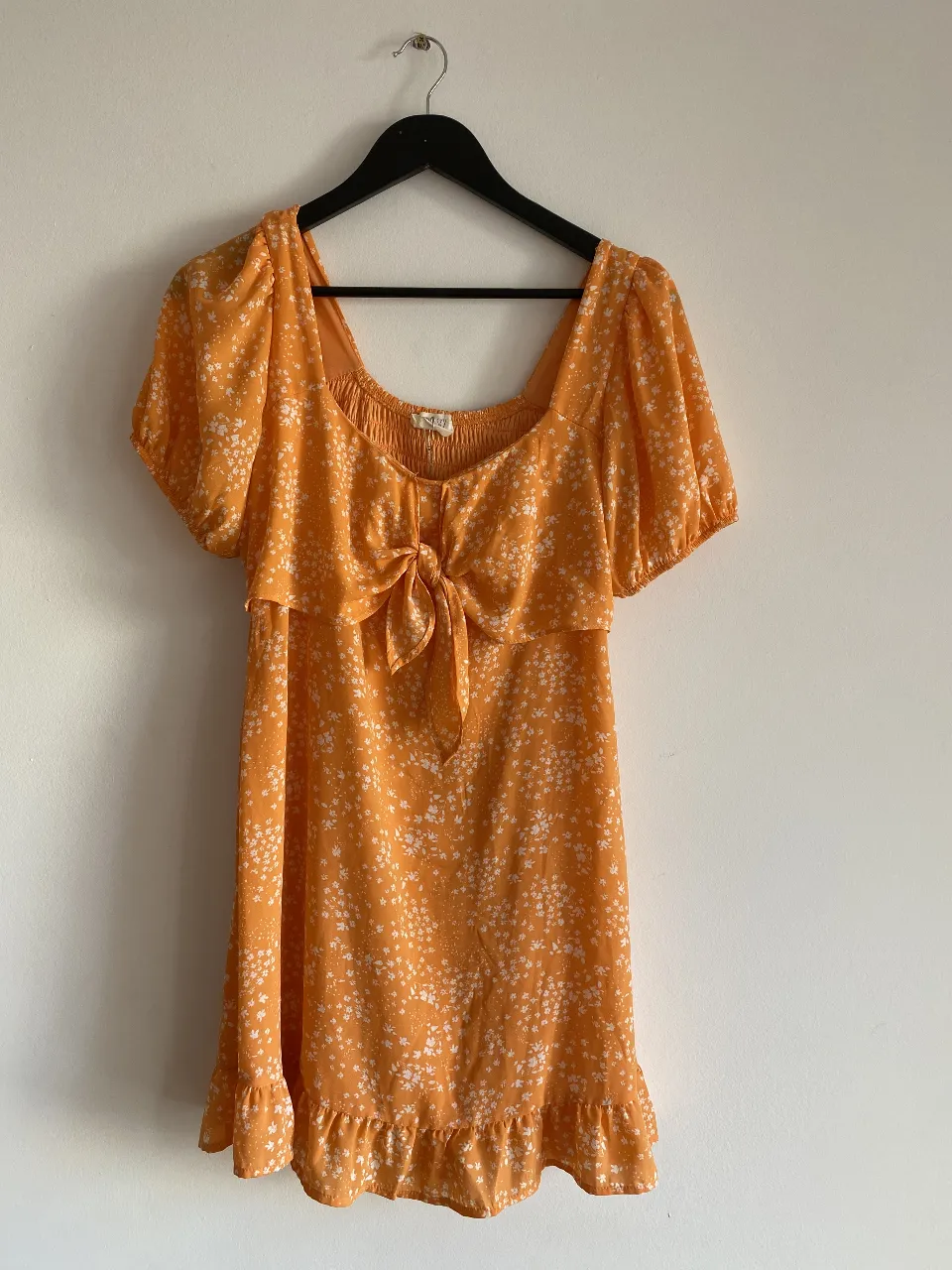 Vestido mini de verano en color amarillo con estampado floral blanco. Diseño con escote cuadrado, mangas cortas abullonadas y detalle de lazo en el pecho. Ideal para un look fresco y femenino.