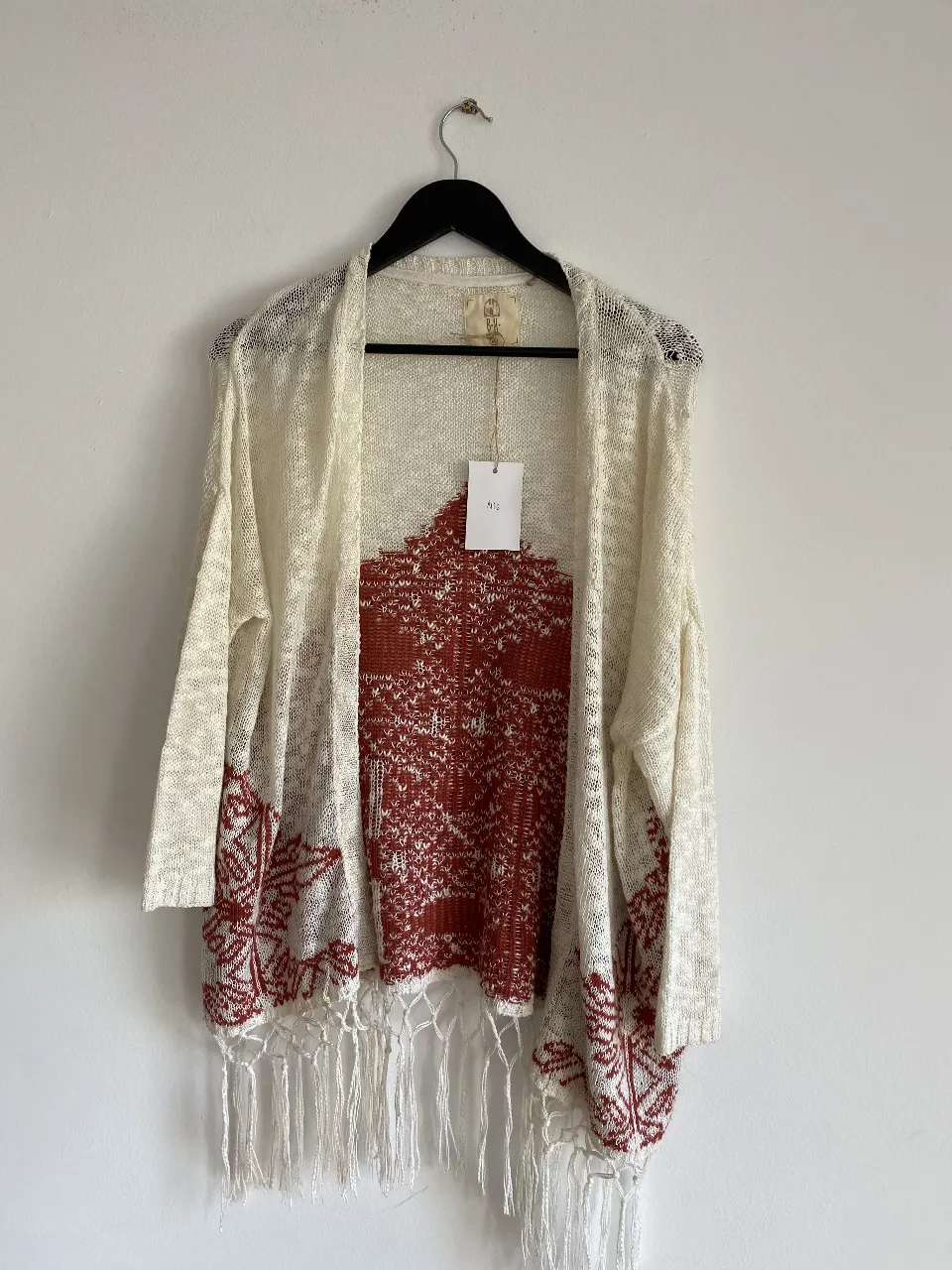 Cardigan tejido con flecos en el bajo, ideal para un look boho chic. Con detalles bordados en rojo y blanco, perfecto para combinar con tus outfits de verano.
