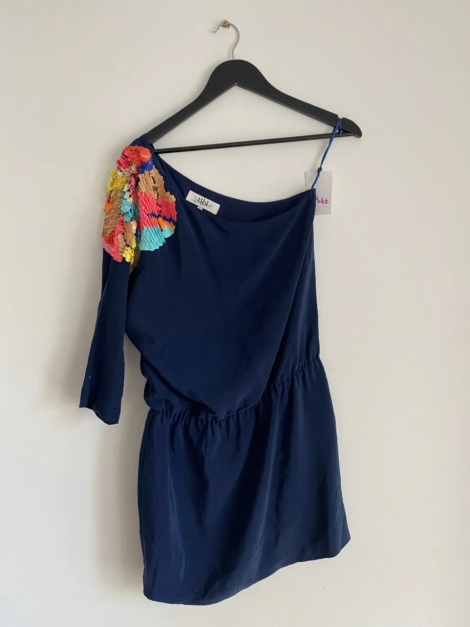 Vestido mini de un solo hombro en color azul marino con detalle de aplique de lentejuelas multicolor en el hombro. Ideal para una fiesta o salida.