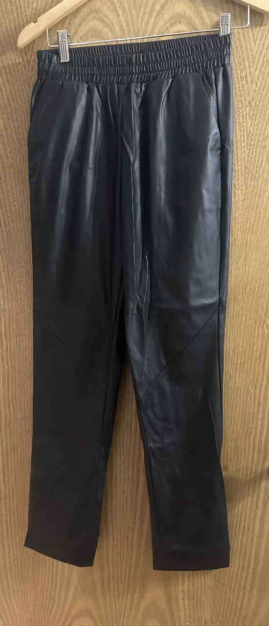 Pantalón sastrero de cuero sintético negro, con cintura elastizada y detalles de costura diagonal en las rodillas. Ideal para un look moderno y sofisticado.
