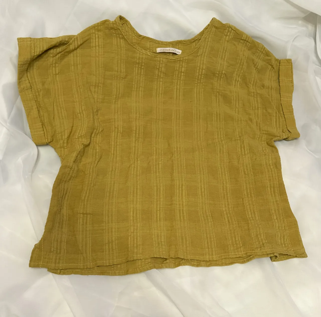 Remera de tela liviana con textura a cuadros finos en color amarillo ocre. Posee mangas cortas y cuello redondo. Ideal para un look casual y fresco.
