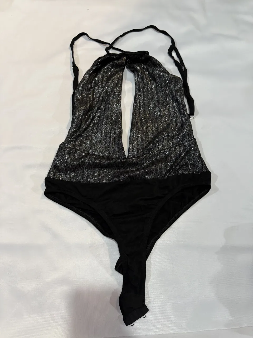 Body súper sensual y llamativo, ideal para una noche de fiesta o para sentirte increíble. Tiene un diseño escotado con tiras que se anudan en el cuello y un detalle cut-out en el frente. La parte superior tiene un brillo plateado que contrasta con la base negra, creando un efecto deslumbrante. La parte inferior es tipo culotte, asegurando comodidad y un calce perfecto.