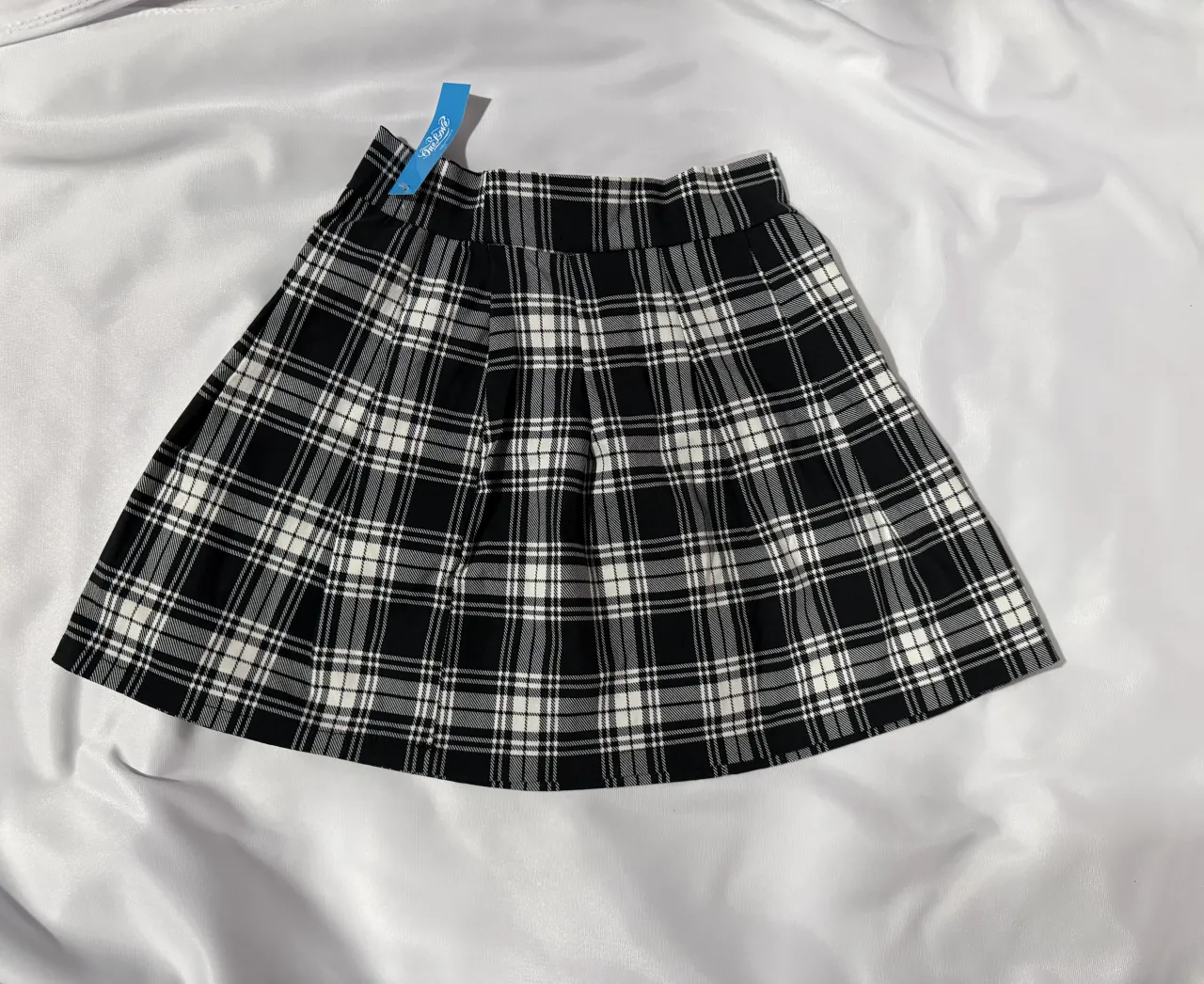 Pollera corta a cuadros escoceses en blanco y negro. Tiene tablas y pretina.