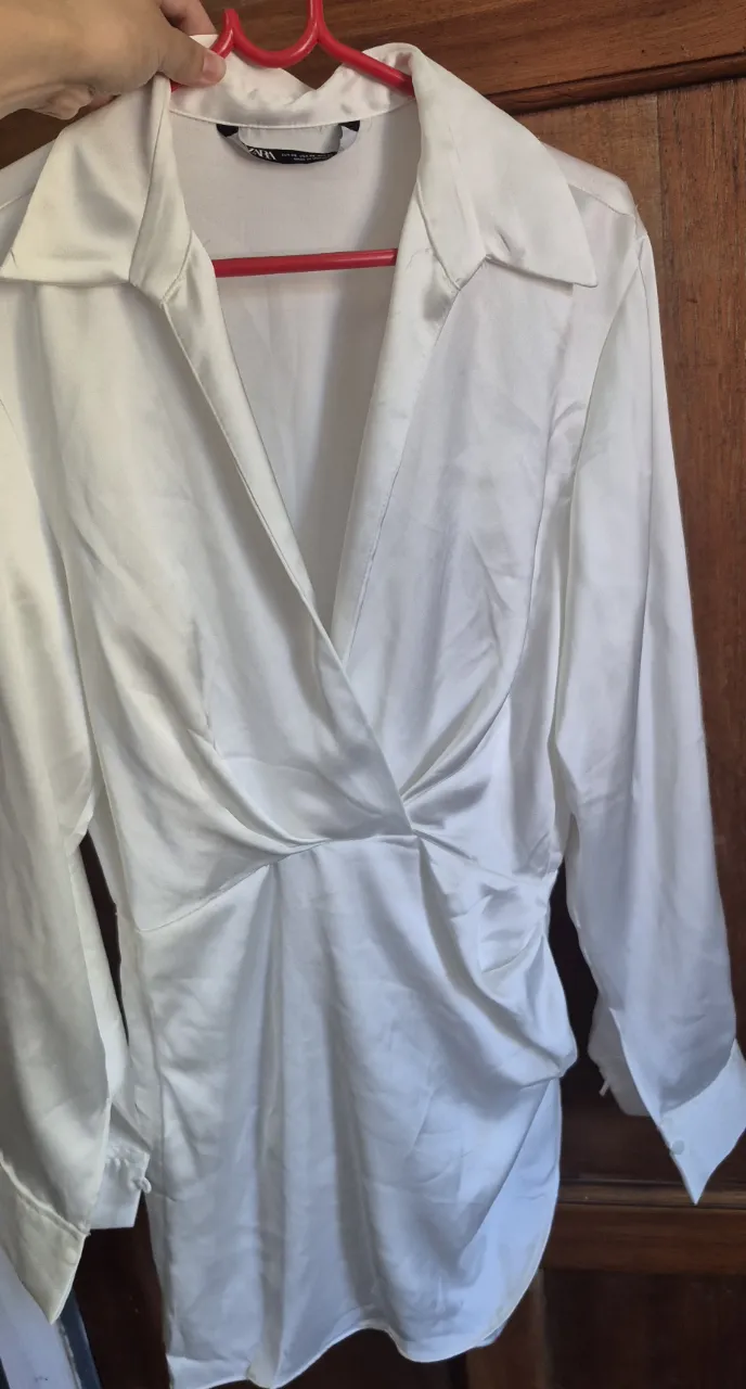 Camisa blanca de seda con escote cruzado y detalle de fruncido en la cintura. Mangas largas con puño. Elegante y versátil, ideal para un look sofisticado.