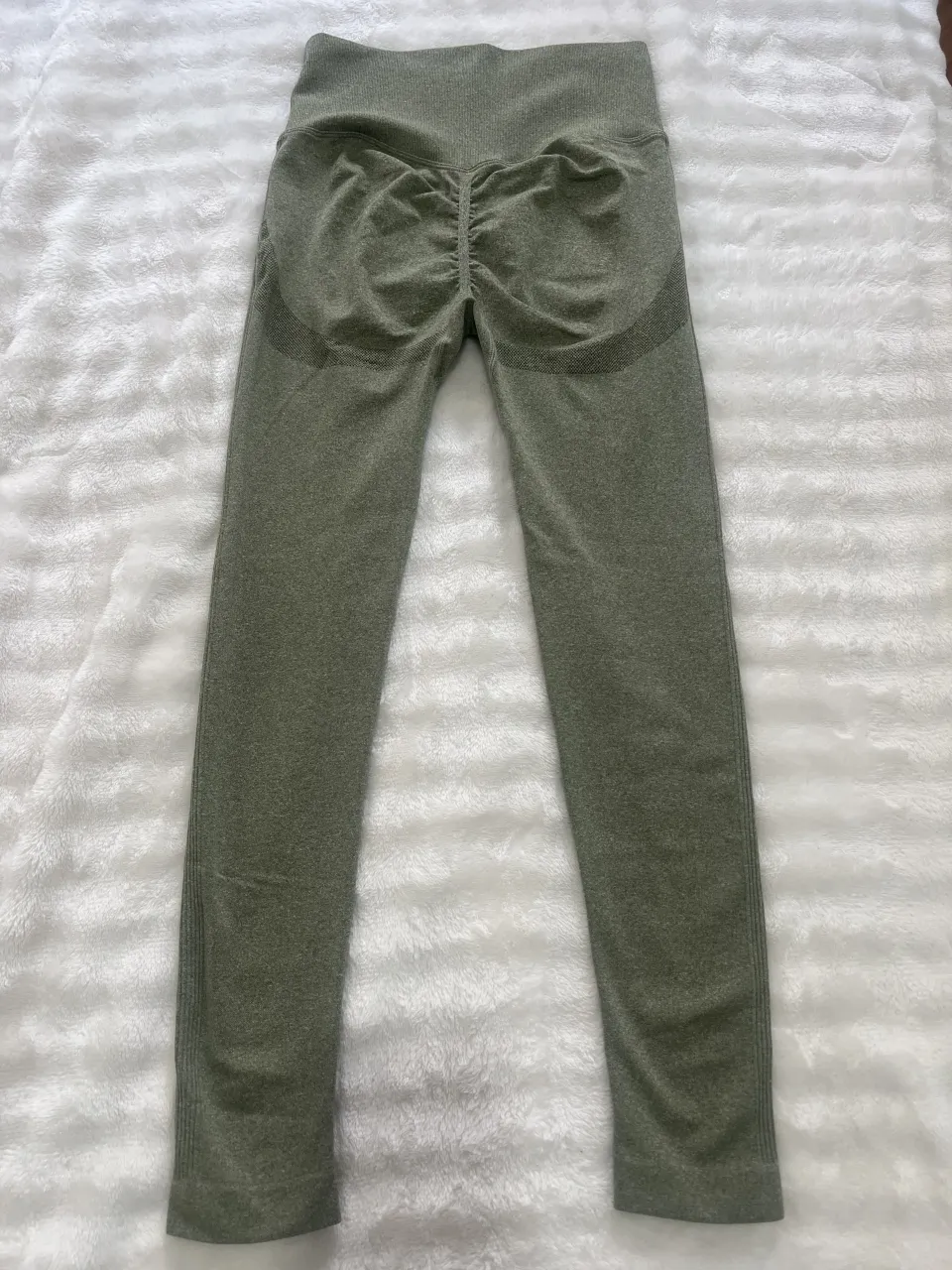 Calzas deportivas color verde musgo con detalles de costuras blancas y fruncido en la parte trasera. Cintura alta.