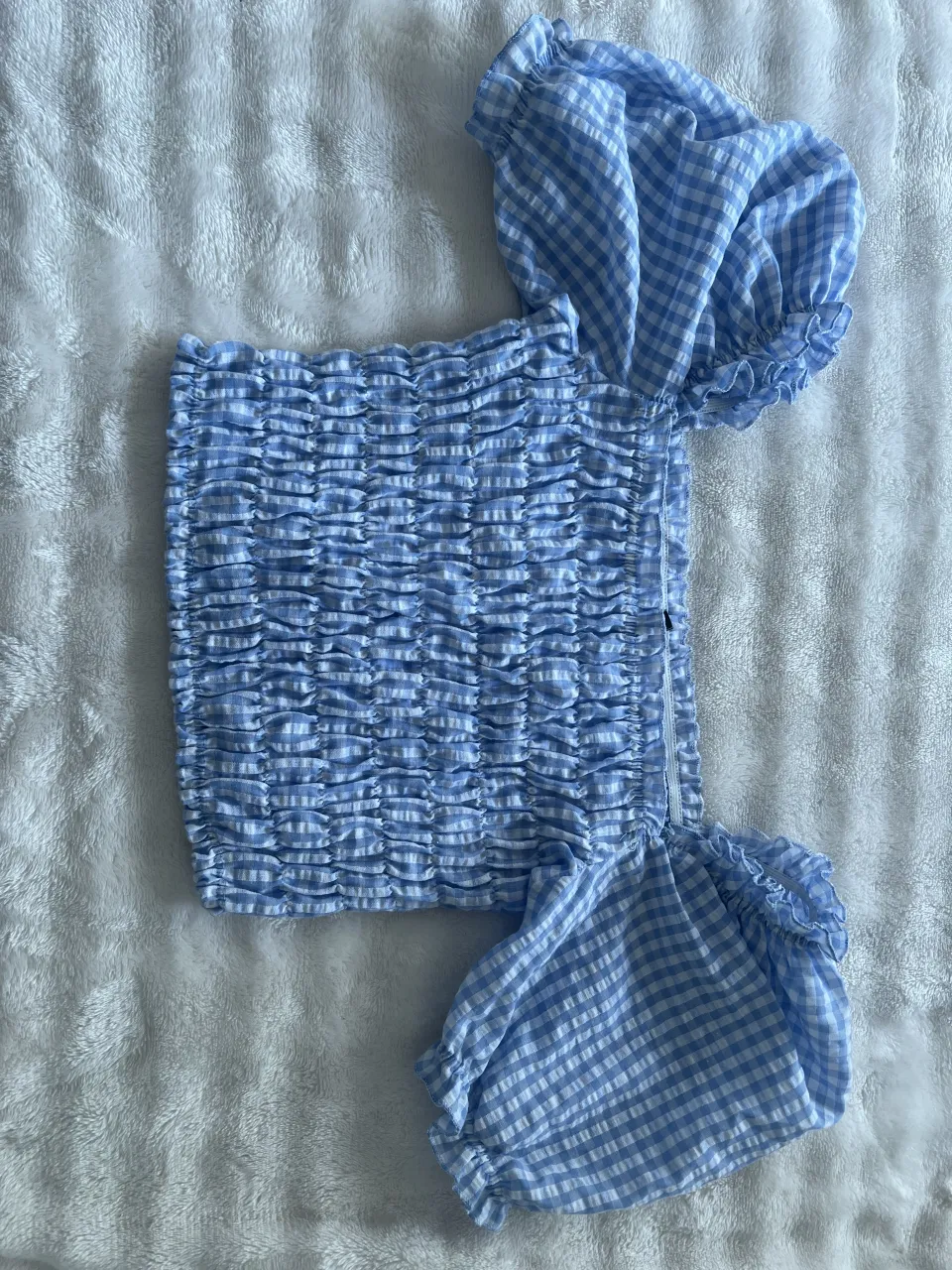 Remera a cuadros celeste y blanco con fruncido en el torso y mangas abullonadas con elástico en los puños.