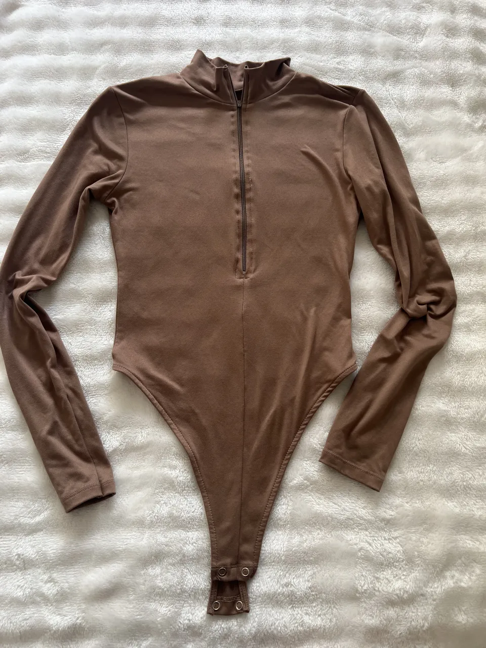 Body de manga larga color marrón con cuello alto y cierre metálico al frente.