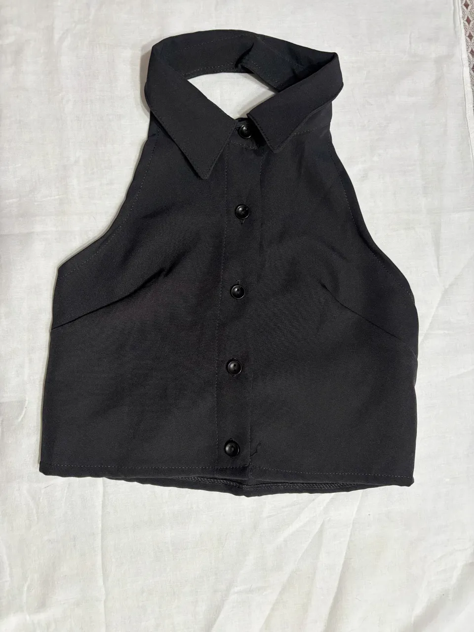 Top negro escotado con cuello camisero y botones al frente. Diseño moderno y canchero, ideal para looks de noche o para darle un toque chic a tu outfit.