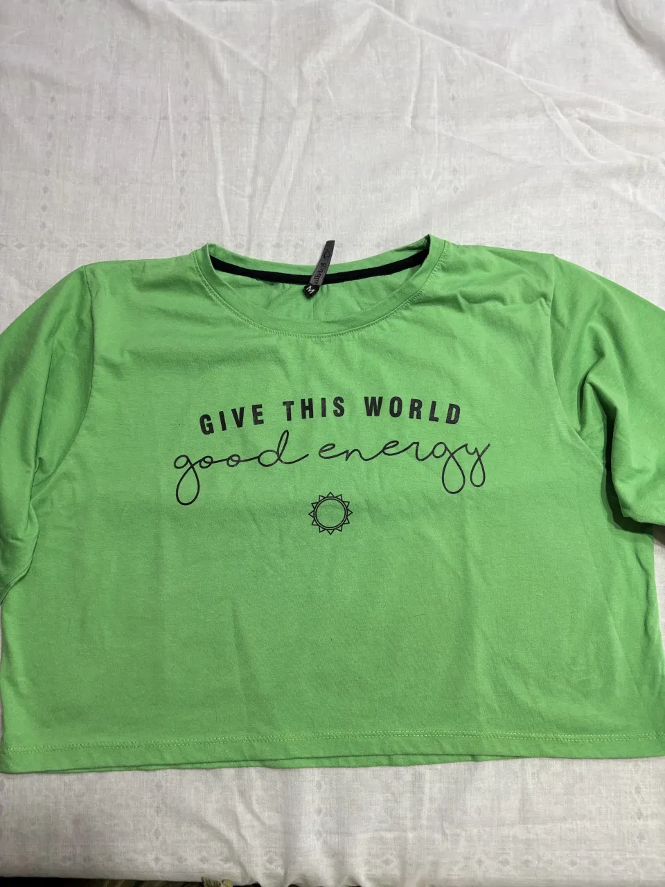 Remera manga corta color verde vibrante con estampa "GIVE THIS WORLD good energy" y un sol. Es un modelo crop, ideal para un look casual y moderno.