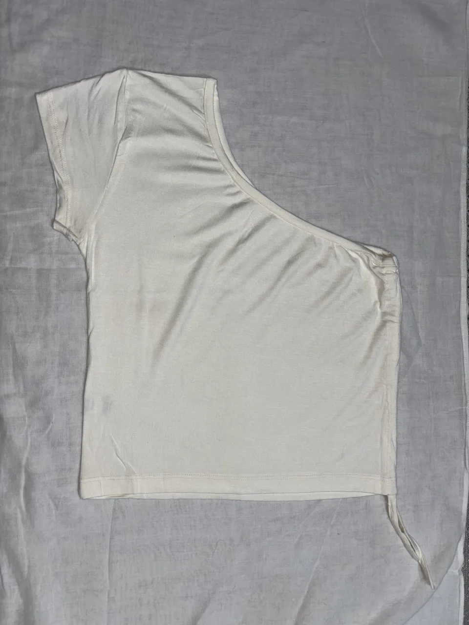 Top blanco asimétrico con detalle de fruncido y tirita lateral. Ideal para un look canchero y moderno.