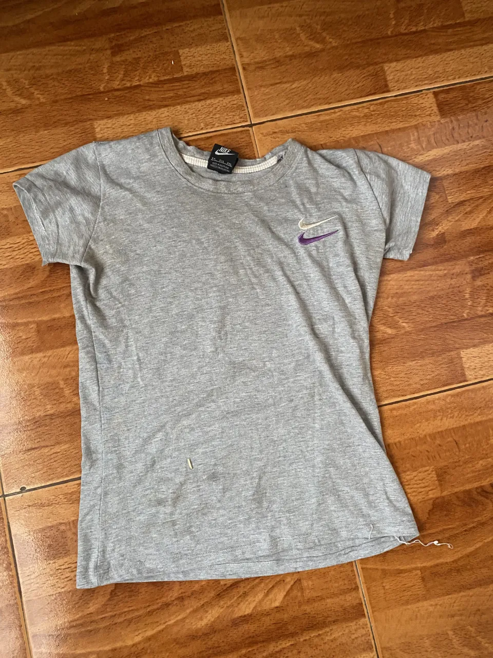 Remera gris de manga corta con logo de Nike en morado. Ideal para entrenar o para un look casual.