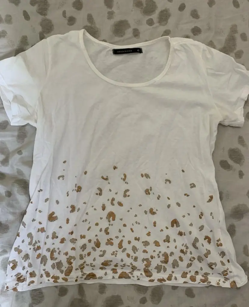 Remera blanca de Cuesta Blanca con estampado de manchas doradas en la parte inferior. Cuello redondo y manga corta. Medidas: axila a axila 45 cm; largo 54 cm; hombro a hombro 35 cm