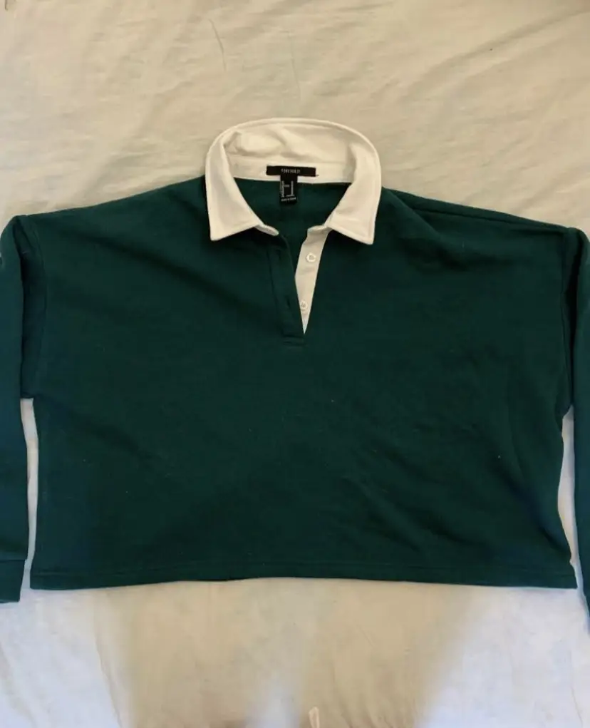 Buzo, de color verde oscuro con cuello blanco tipo polo. De la marca Forever 21, talle M.            Medidas: axila a axila 65 cm; largo 50 cm; largo manga 46 cm.