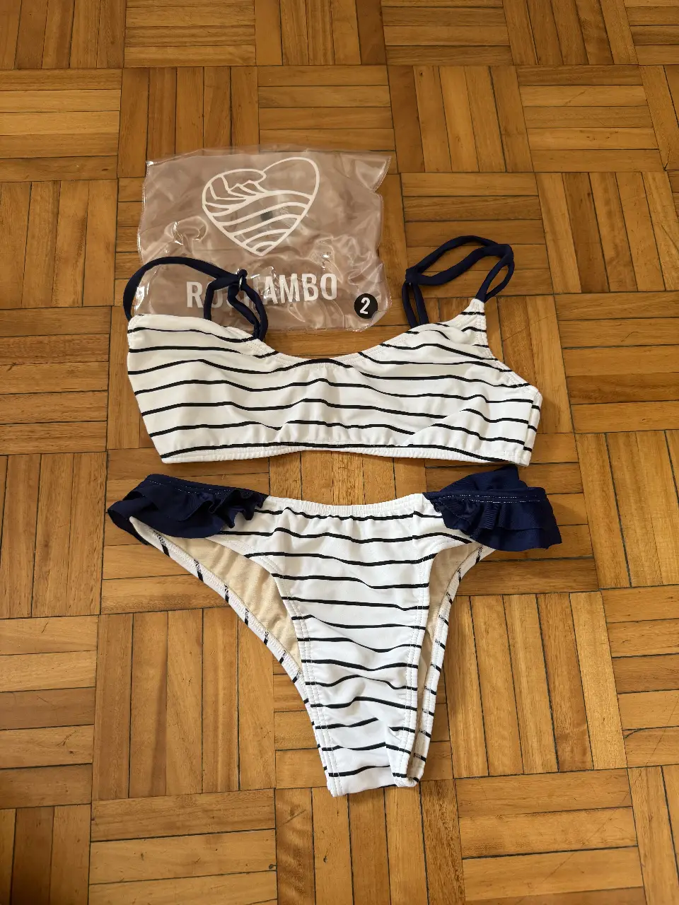 Conjunto de bikini a rayas blancas y negras con detalles en azul marino. Incluye corpiño con tirantes y bombacha con volados.