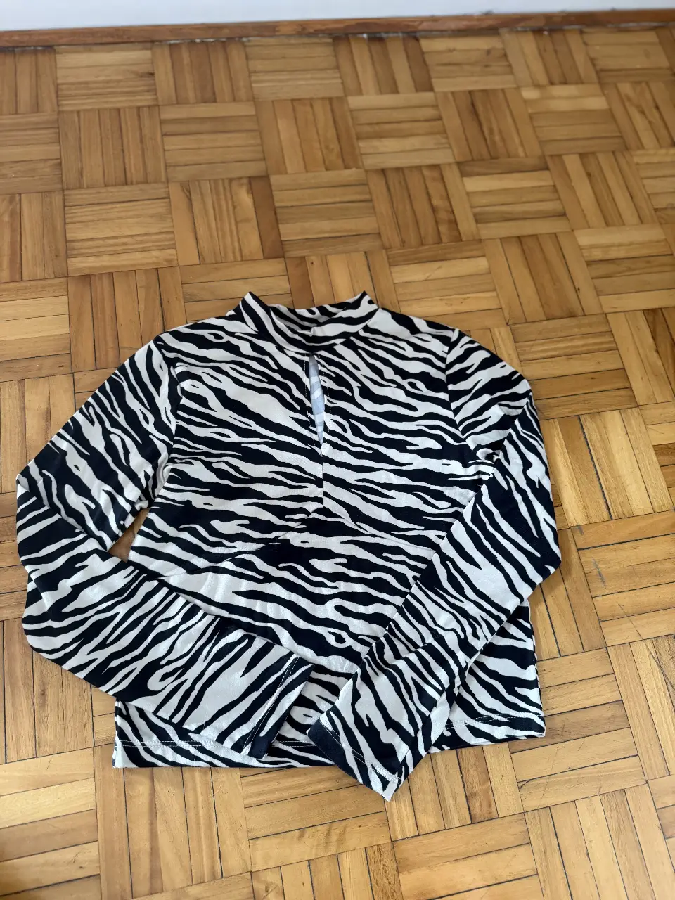 Blusa de manga larga con estampado de cebra en blanco y negro. Cuello alto y cierre frontal.