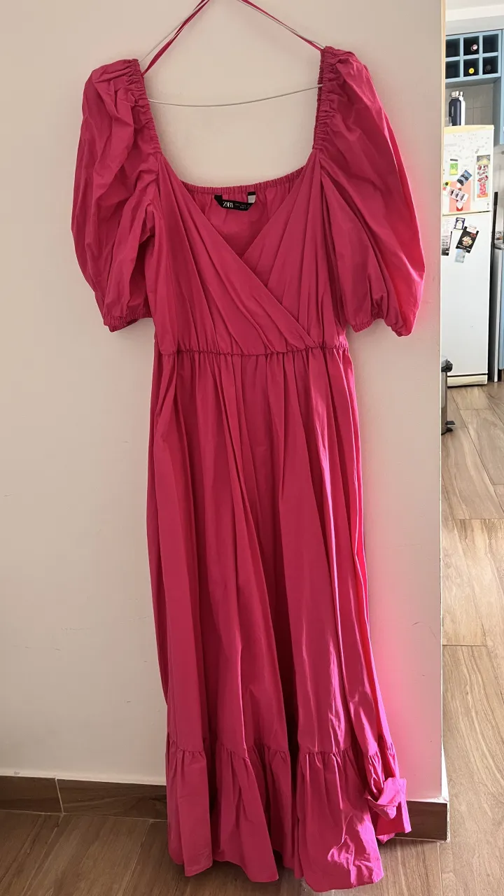 Vestido rosa con escote cruzado y mangas cortas abullonadas. Posee elástico en la cintura y volado en el ruedo.