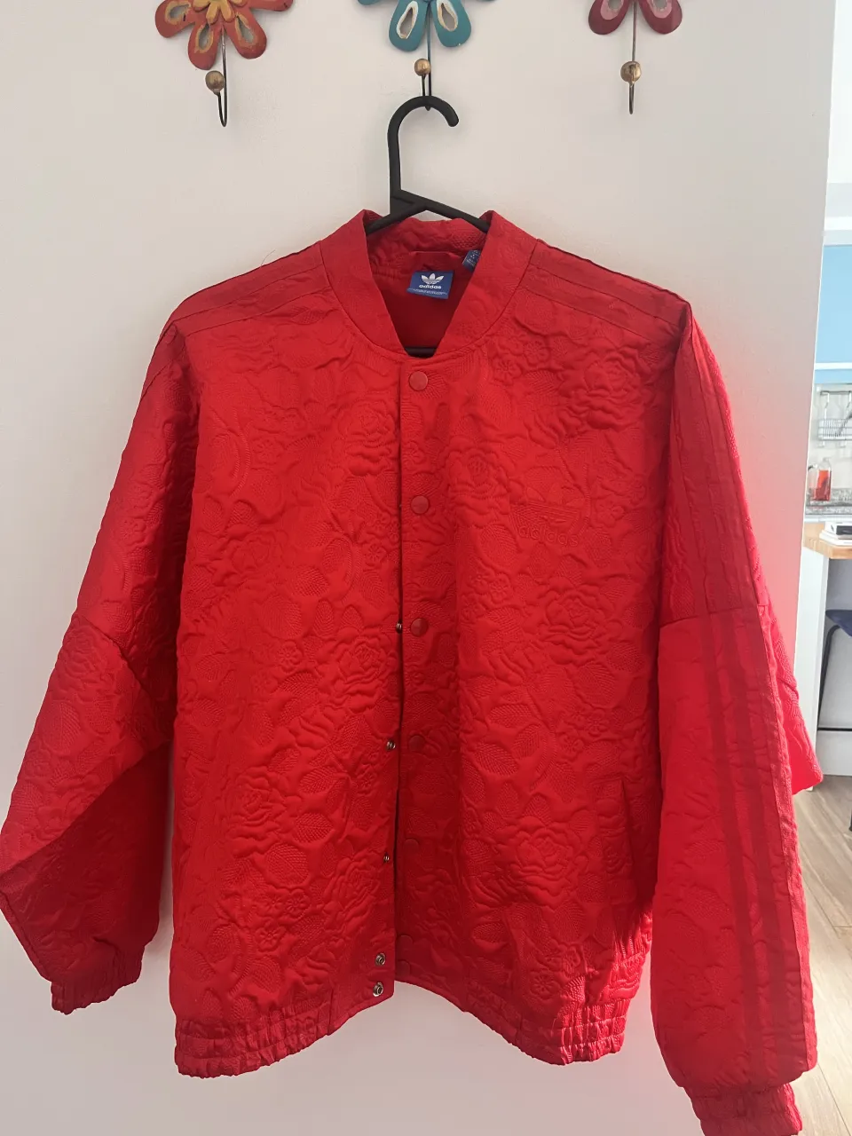 Campera bomber roja con textura floral y logo de Adidas bordado en el frente. Cierre de broches.