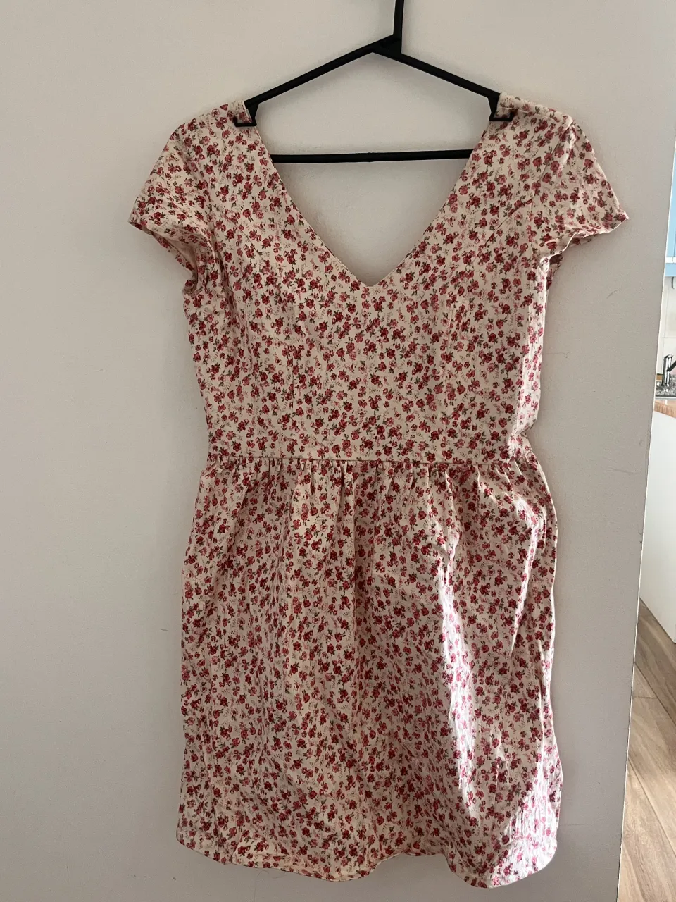 Vestido corto estampado con flores pequeñas en tonos rojos y rosas sobre fondo blanco. Escote en V y mangas cortas.