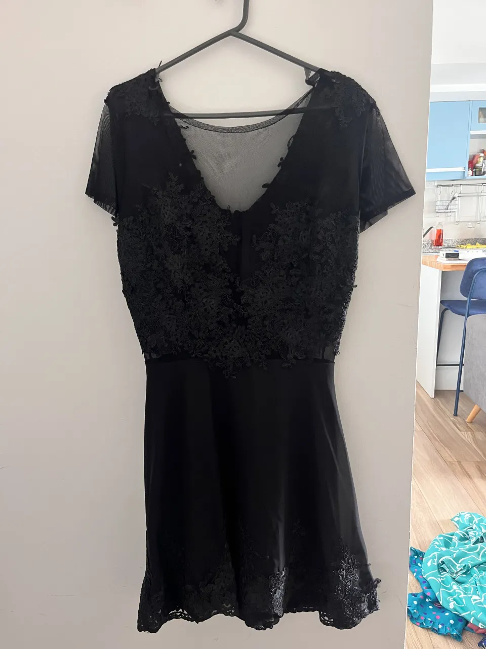 Vestido negro corto con detalles de encaje floral en el escote y en el borde inferior. Escote en V con transparencias.