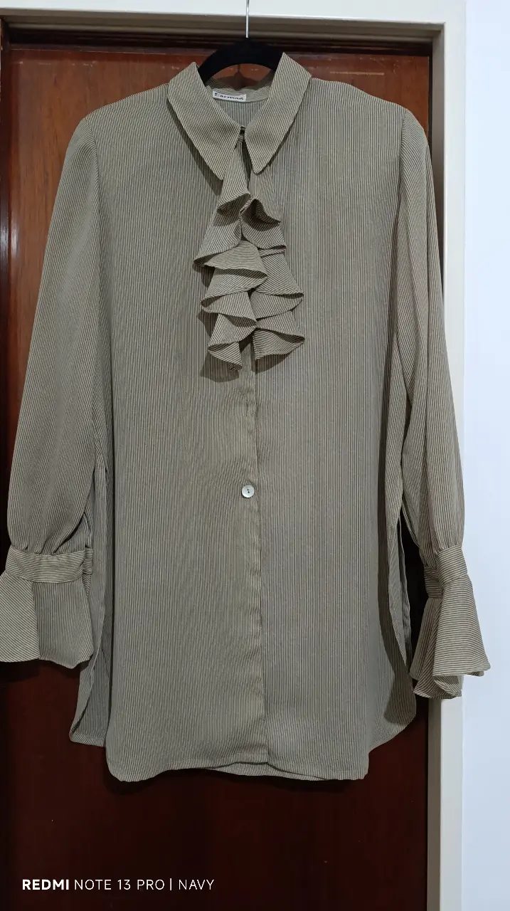 Blusa de mujer a rayas verticales en color marrón. Presenta un diseño elegante con volantes en el frente y mangas largas con puños acampanados. Ideal para un look sofisticado.