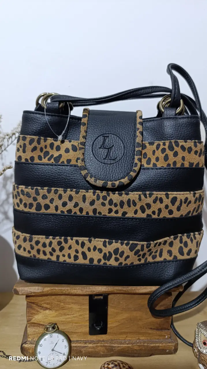 Cartera bandolera con diseño de franjas negras y detalles de estampado de leopardo. Cuenta con un cierre de solapa y un asa ajustable para llevar al hombro. Ideal para un look casual y moderno.