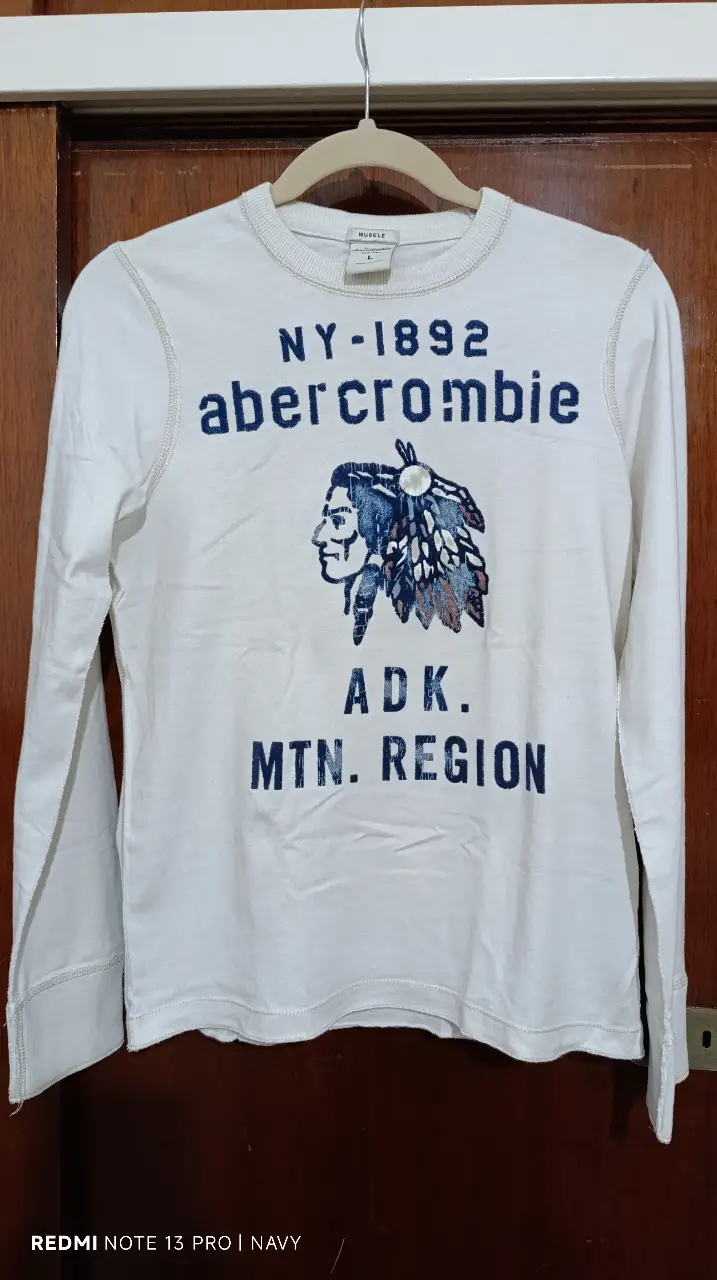 Remera manga larga Abercrombie & Fitch, blanca con estampado azul en el frente. Talle L. Ideal para un look casual y cómodo.