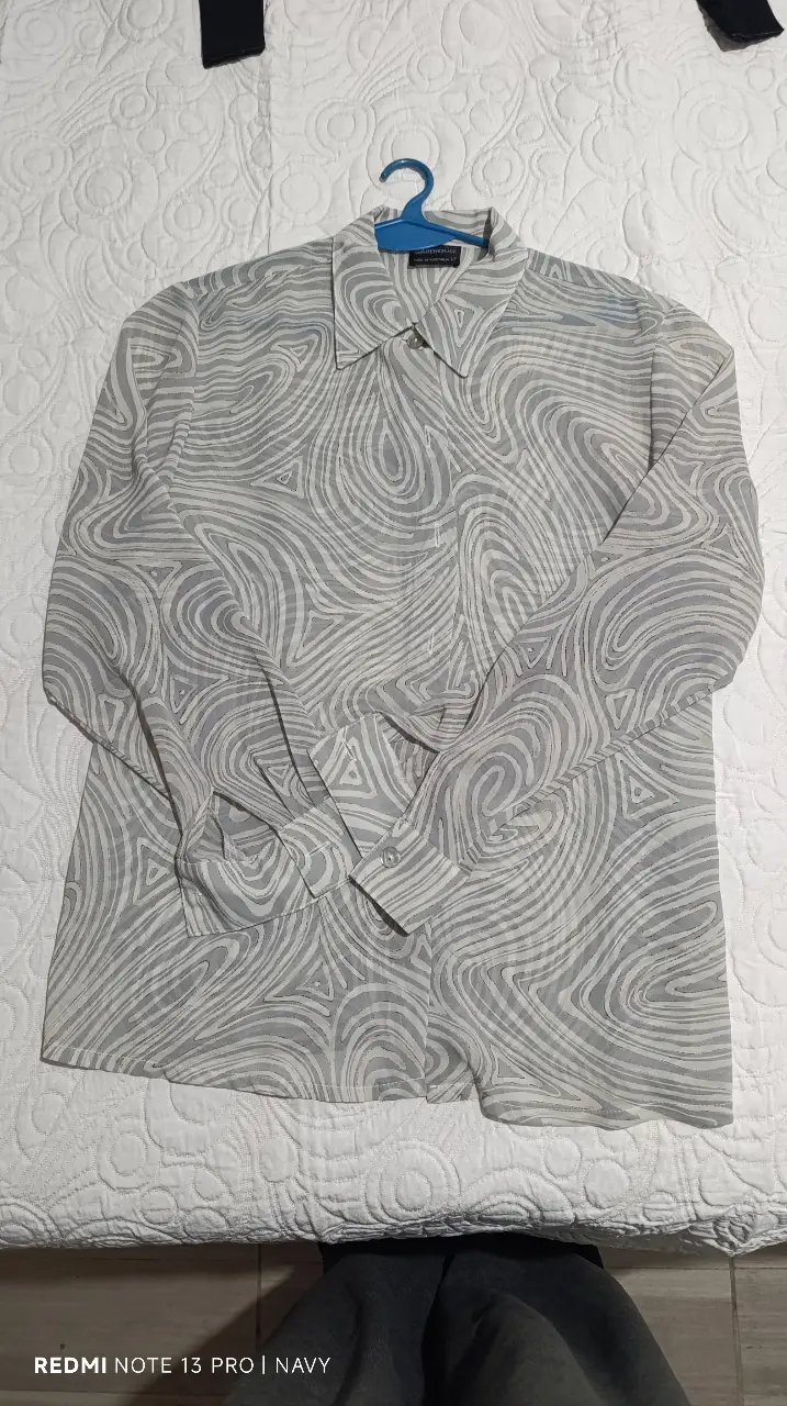 Camisa estampada con diseño abstracto en tonos grises y blancos. De manga larga, con cuello clásico y puños con botones. Ideal para un look casual y moderno.