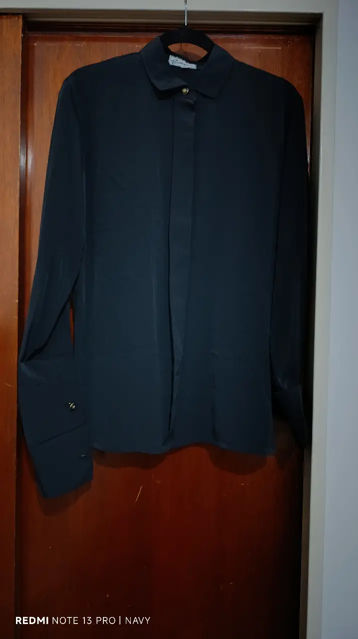 Blusa de manga larga negra de la marca Paradigmas. Confeccionada en un tejido suave y elegante, esta camisa presenta un diseño clásico con cuello camisero y puños con botones. Ideal para un look sofisticado y versátil.