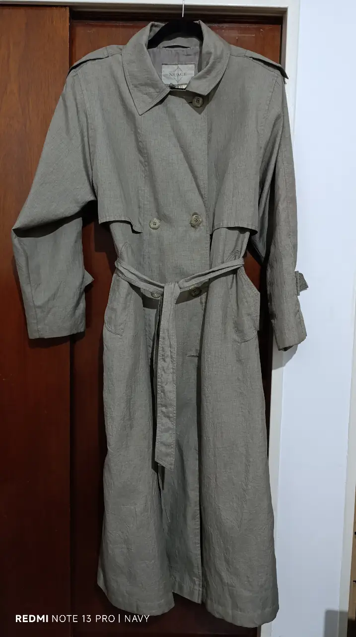 Trench coat de color gris, con cinturón y botones. Ideal para un look elegante y sofisticado. Perfecto para la temporada de otoño/invierno.