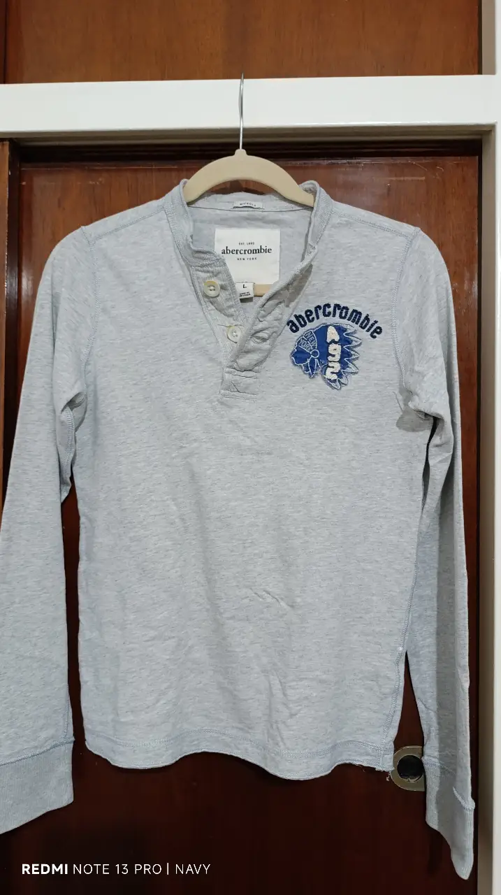 Remera manga larga de adolescente Abercrombie, color gris claro, con cuello redondo y botones. Estampado en el pecho.