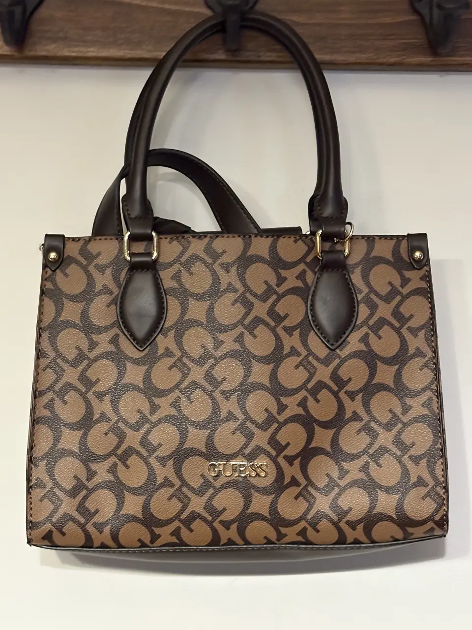 Cartera Guess con estampado del logo de la marca en color marrón y detalles dorados. Ideal para llevar tus esenciales con estilo.