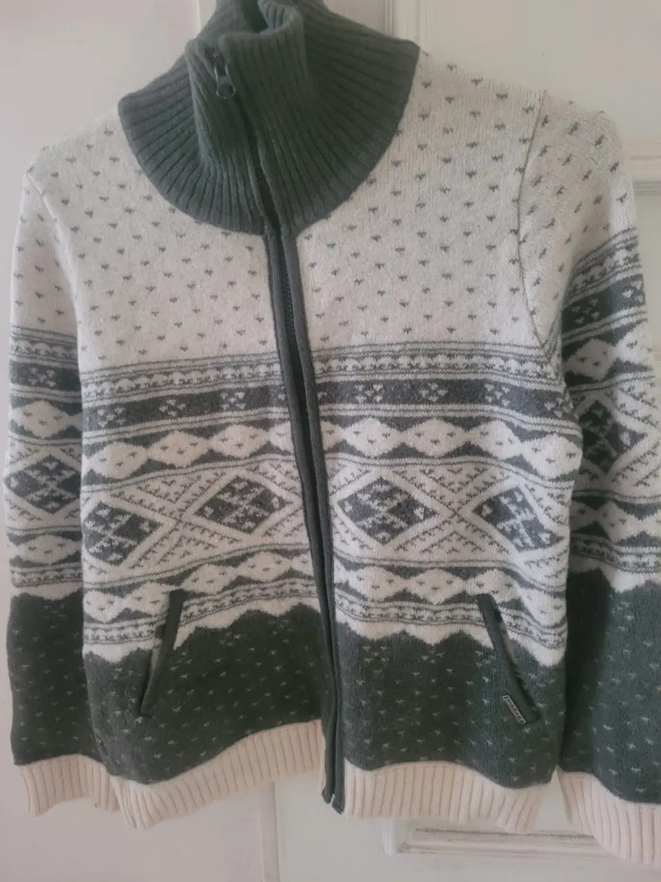 Sweater de cuello alto con cierre y diseño de rombos en gris, verde y blanco. Ideal para el invierno, con bolsillos y detalles tejidos.