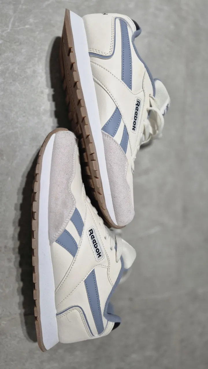 Zapatillas deportivas Reebok de cuero y gamuza en color blanco tiza con detalles en azul claro. Logo de la marca en los laterales y en el talón.