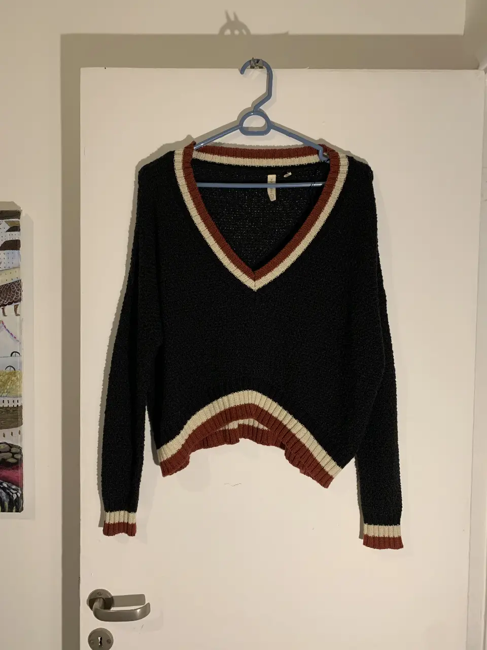 Sweater negro con cuello en V y detalles en blanco y rojo. Ideal para un look casual y abrigado.