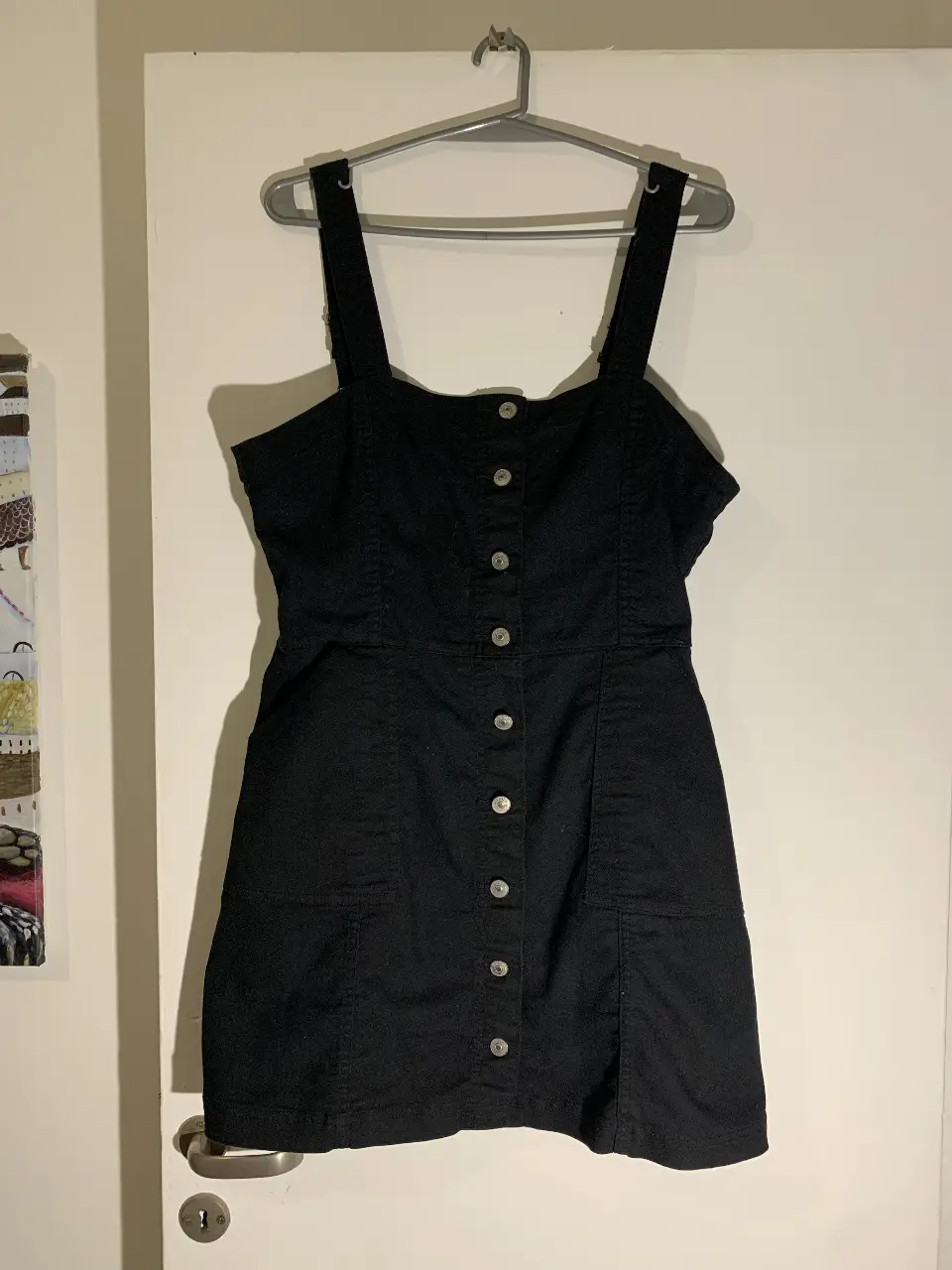 Vestido mini negro con botones delanteros y tirantes ajustables. Ideal para un look casual y moderno. Es tipo jumper para usar con remera debajo. De tela tipo jean pero un poco más flexible. 
