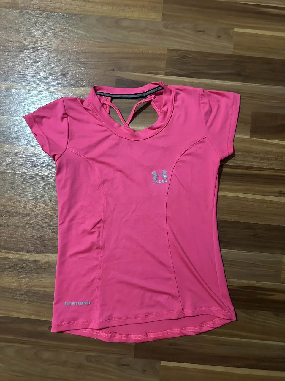 Remera deportiva rosa de mujer, con espalda descubierta y detalle de diseño. Ideal para entrenamientos y actividades físicas. Marca Under Armour.