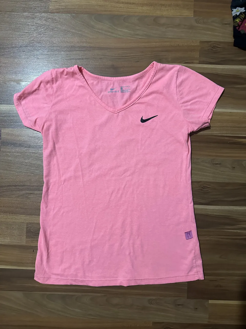 Remera deportiva Nike Dri-Fit rosa, con logo negro. Ideal para entrenar.