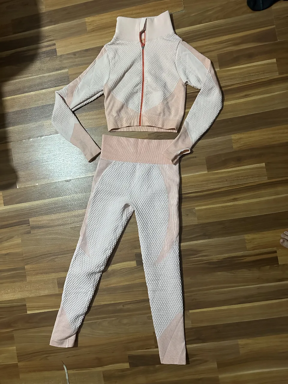 Conjunto deportivo de mujer, compuesto por campera de manga larga con cierre y calzas. Diseño texturizado en tonos blanco y rosa. Me quedo pequeño 