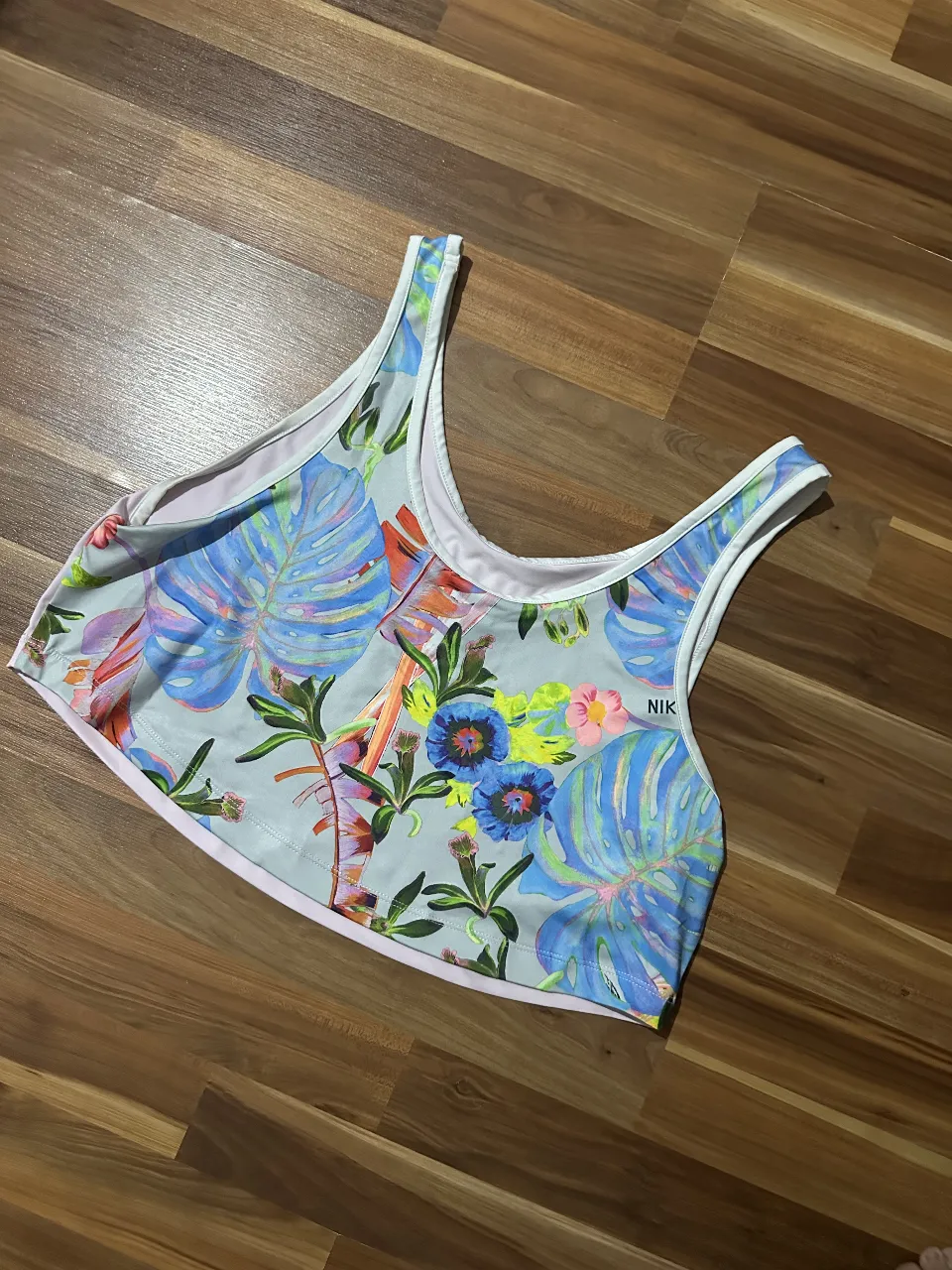 Top deportivo Nike con estampado floral y logo. Ideal para entrenamientos y actividades de verano. Diseño moderno y cómodo.