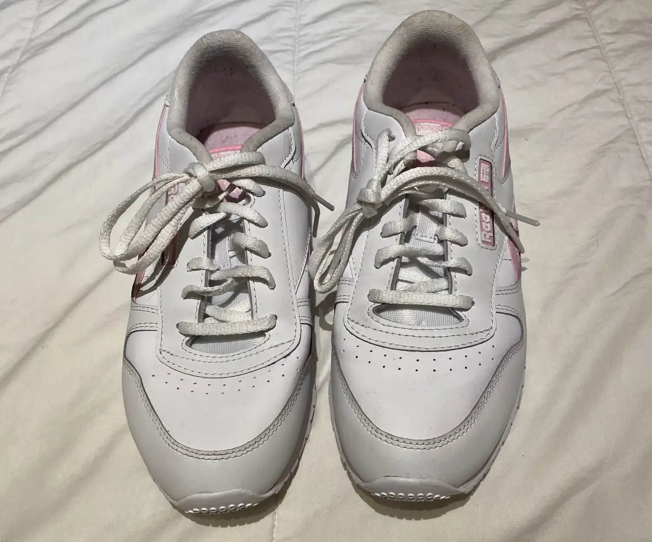 Zapatillas Reebok blancas con detalles en rosa, ideales para un look casual y cómodo. Tienen cordones blancos y el logo de la marca en el lateral. Perfectas para el día a día.