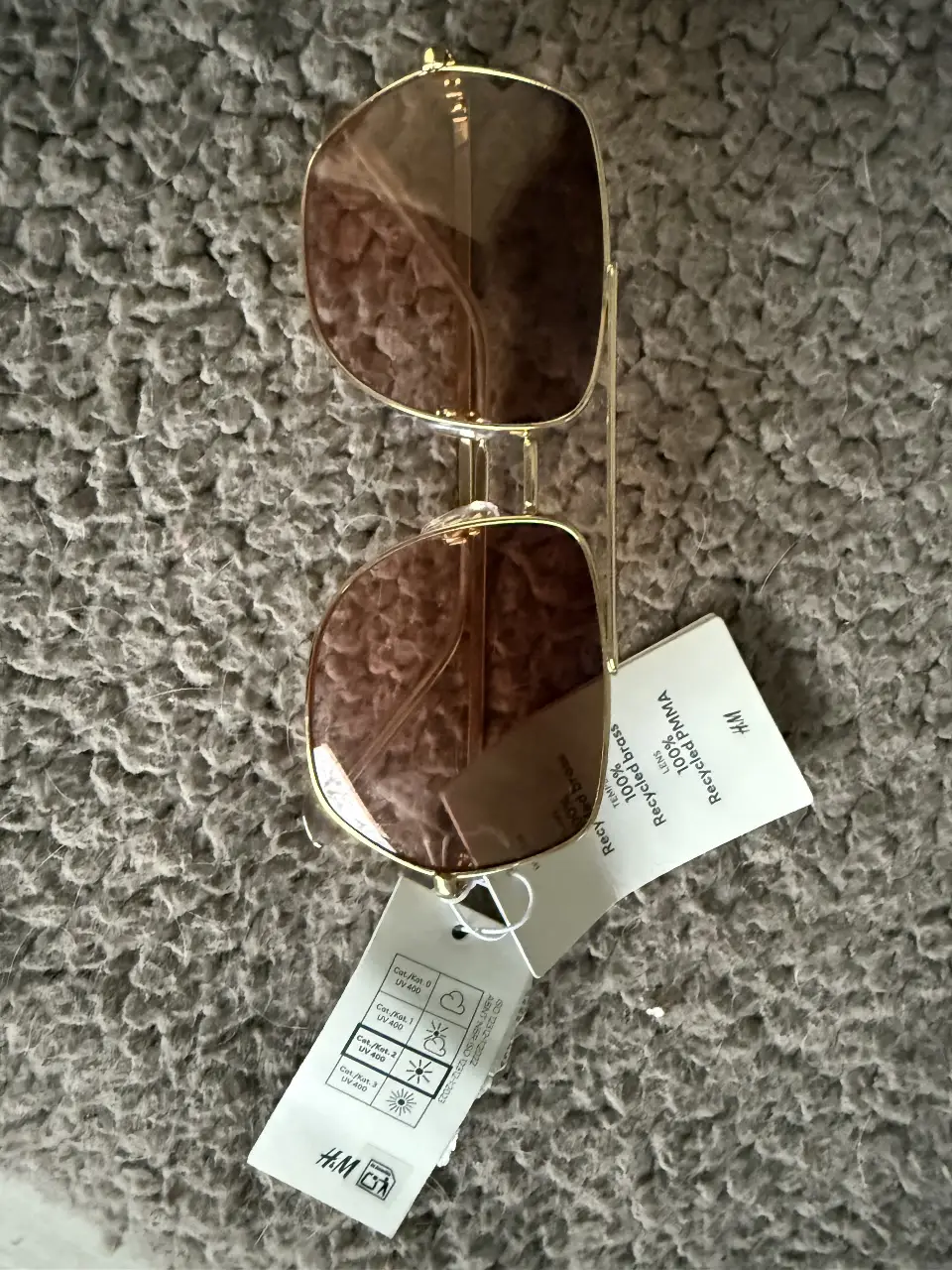 Anteojos de sol dorados con cristales marrones, estilo aviador, con etiqueta de la marca H&M.