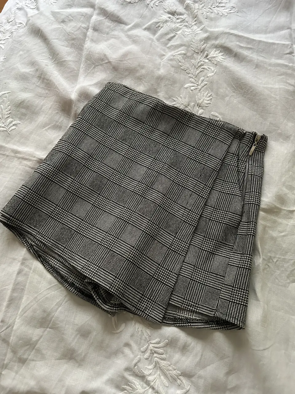 Shorts de mujer con estampado a cuadros en tonos grises y blancos. Diseño con corte tipo polleras-pantalón, cierre lateral y detalle de solapa. Ideal para un look casual y moderno.