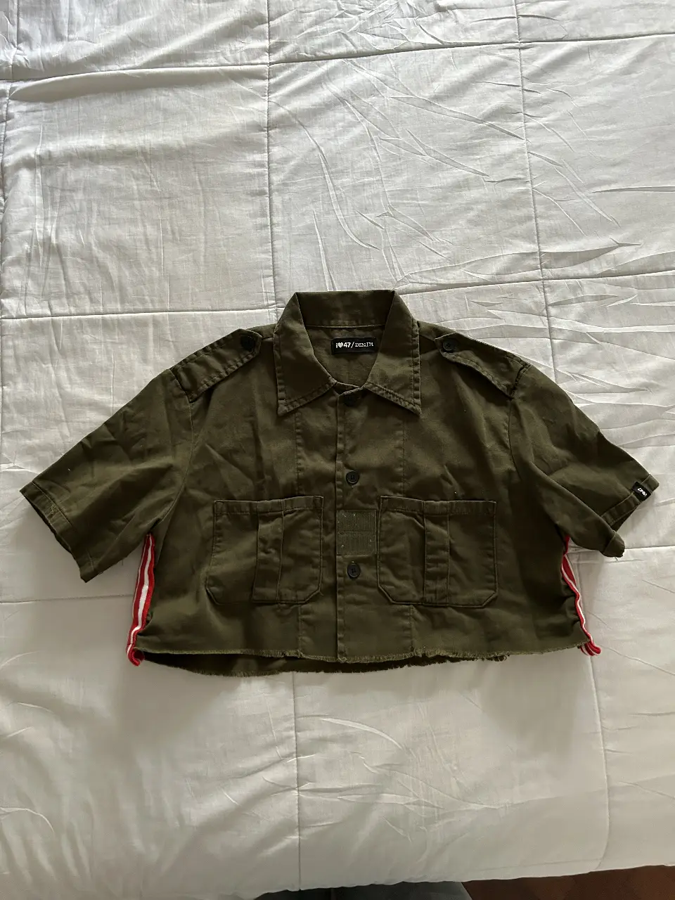 Camisa crop verde militar con detalles en rojo y blanco en los laterales. Corte cropped, ideal para un look casual y canchero.