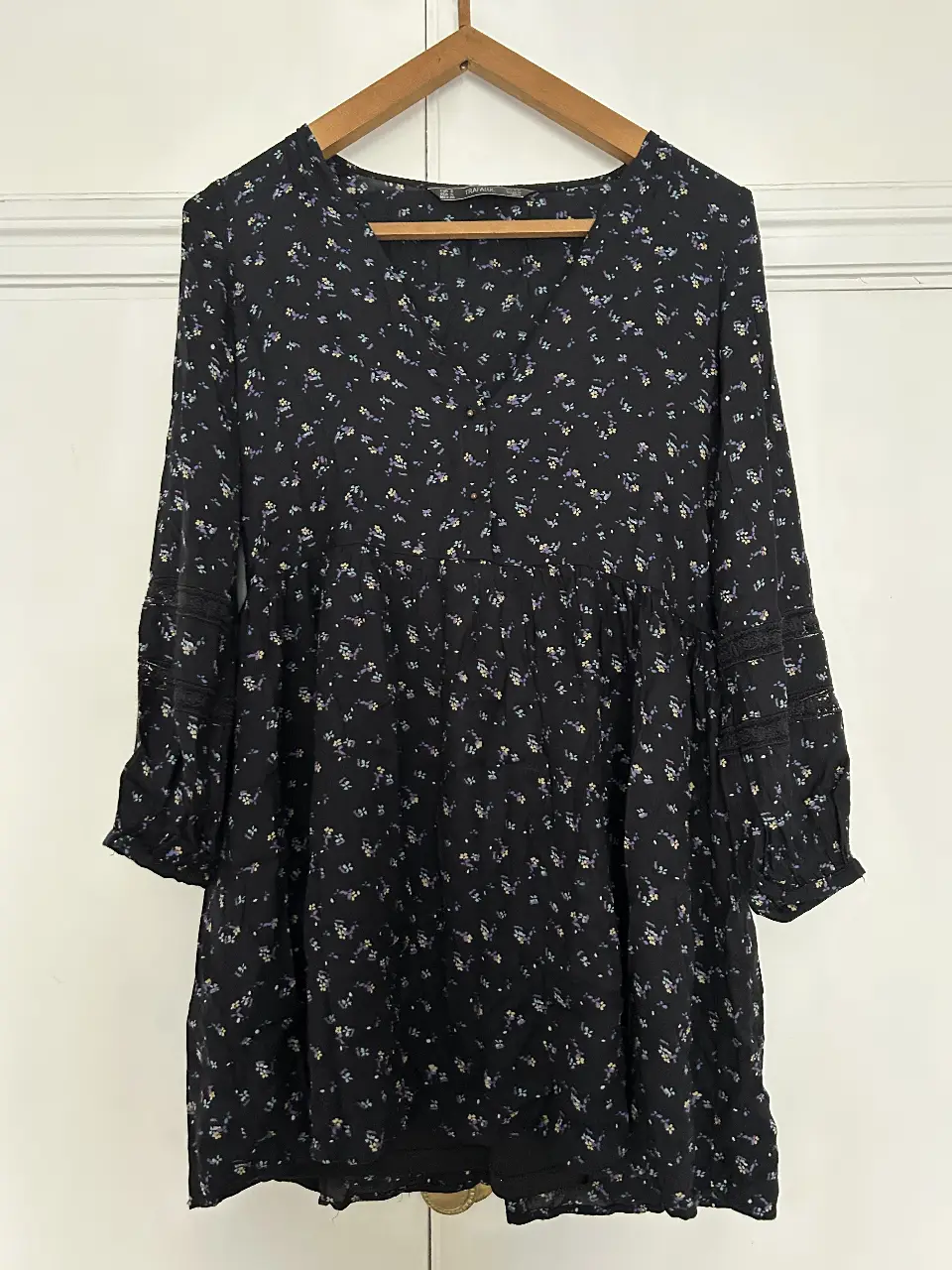 Vestido midi negro con estampado floral. Tiene mangas largas con detalles de encaje y un corte en la cintura que le da un estilo romántico y femenino. Ideal para un look casual o para una salida.