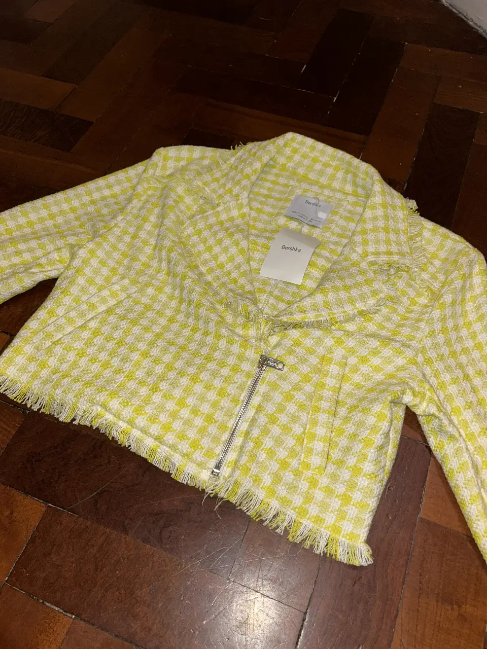 Campera bomber de Bershka, con diseño a cuadros en amarillo y blanco. Tiene cierre y flecos en el borde inferior y en el cuello. Talle M/L.