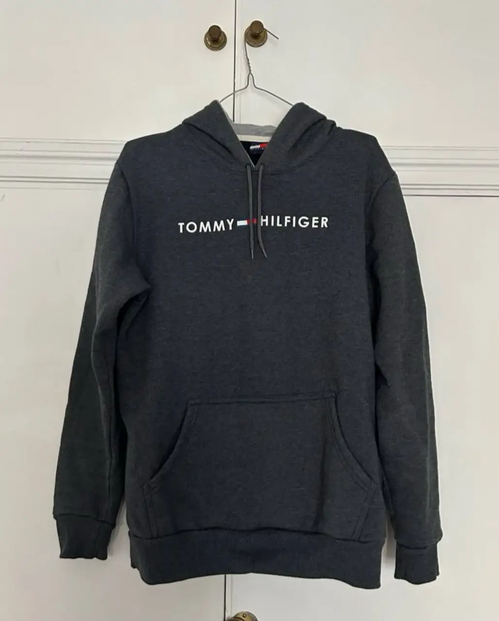 Buzo canguro de hombre Tommy Hilfiger, color gris oscuro, con el logo de la marca en el pecho. Ideal para un look casual y cómodo ✨ Medidas: espalda 46cm, de axila a axila 56cm, largo total desde hombro 67cm, largo de manga 63cm