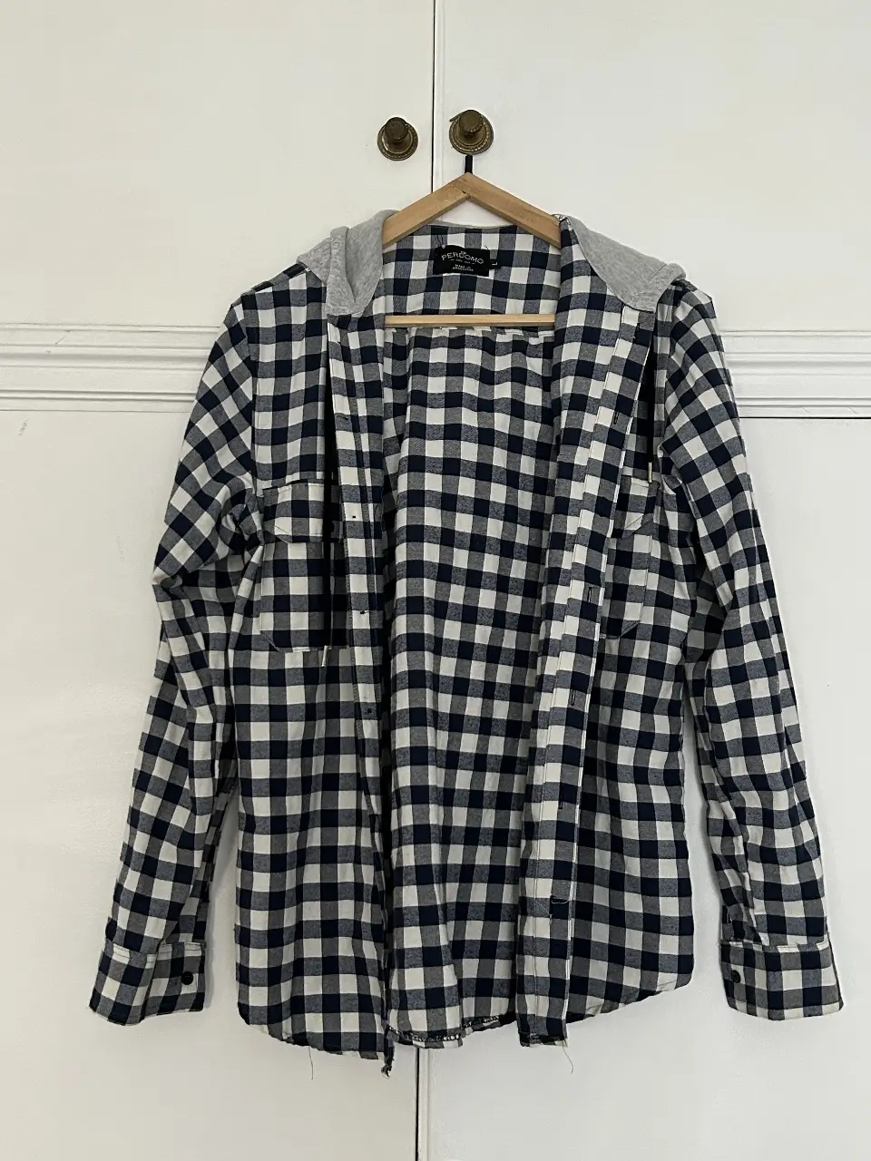 Camisa a cuadros con capucha de color gris. La camisa es de manga larga y tiene un bolsillo en el pecho. Ideal para un look casual y moderno.