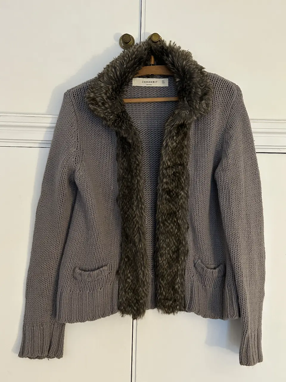 Cardigan Zara de lana gris con detalle de piel sintética en el cuello y borde frontal. Ideal para un look casual y abrigado en invierno.