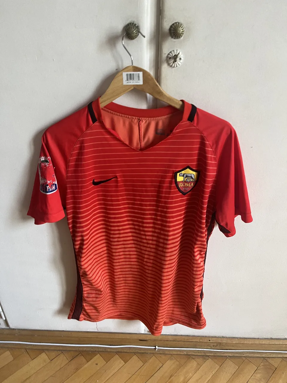 Camiseta de fútbol AS Roma, color rojo con detalles en negro y logo de Nike. Diseño con líneas horizontales y el número 10 en la espalda.